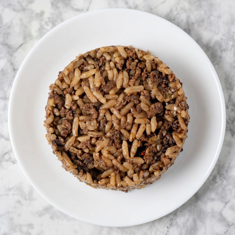 Top-down view of a white plate with a circular serving of brown rice and ground meat.